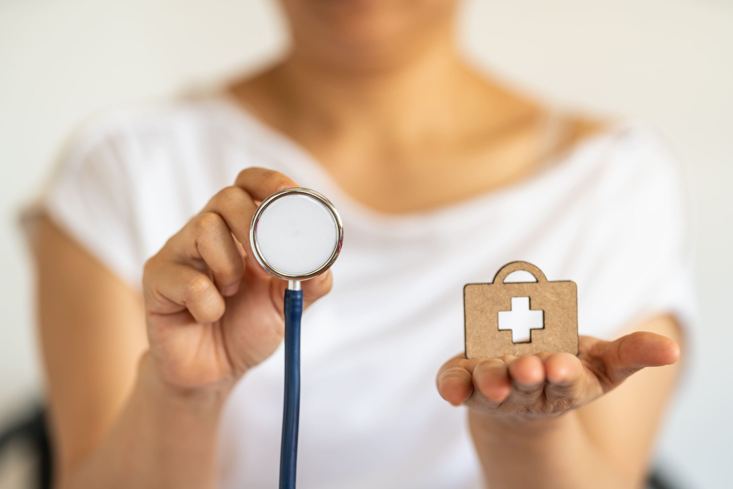 people-healthcare-concept-closeup-woman-hand-holding-stethoscope-with-wooden-diecut-bag-with-medical-cross-logo (1) (1)